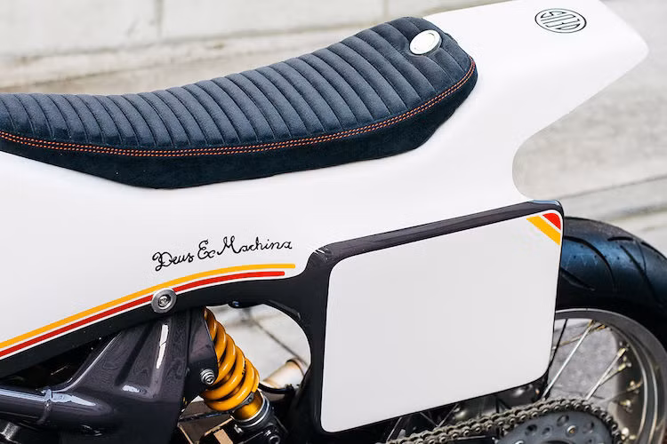 Trong khi đó, phần khung phụ phía sau nguyên bản của VTR250 đã được cắt bỏ, sau đó khéo léo tích hợp một bình xăng nhỏ vào phía đuôi xe. Nắp xăng có khả năng đóng mở nhanh và nằm ngay phía sau bộ yên phẳng, được bọc bằng vải nhung Alcantara. Toàn bộ thân xe được sơn màu trắng với các vạch kẻ mang hơi hướng cổ điển.