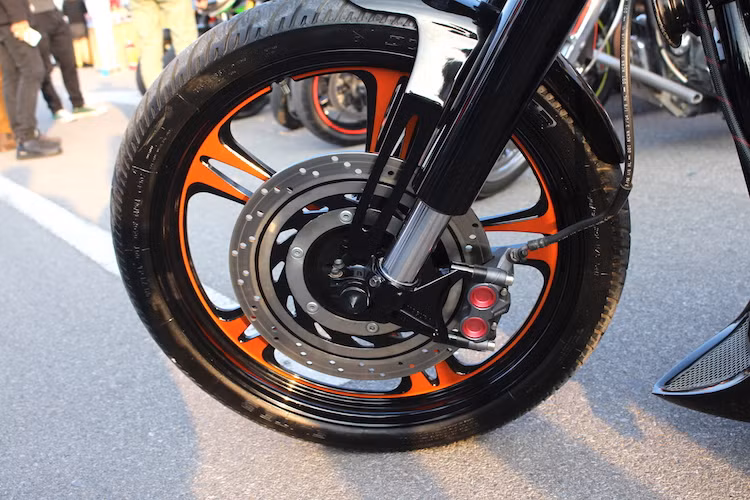 Chưa dừng lại ở đó, "dàn chân" trước của xe cũng đã được độ mâm 5 cánh kép với tông màu đen đỏ và có đường kính lên tới 21 inch. Đi kèm với mâm độ là lốp Dunlop với kích thước 90/80/21. Đĩa trước nguyên bản của VTX1300 được giữ lại, nhưng có heo phanh nâng cấp lên loại 4 piston radial an toàn hơn.