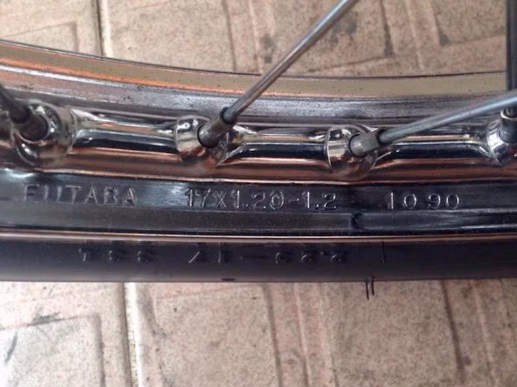 "Soi kỹ" hơn ở bánh trước, có thể thấy chiếc xe vẫn còn giữ được bộ lốp còn gai gió kèm vành sắt mạ được sản xuất bởi hãng Futaba - Nhật Bản. Con số "1090" trên vành đã cho thấy nó được sản xuất vào tháng 10 năm 1990. Đây là một dấu hiệu tốt để nhận biết đời của chiếc xe. Ngoài Cub, dòng Dream II "tem hồng 3 cục" nguyên bản cũng có date sản xuất dập trên vành trước.