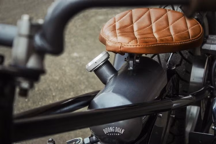 Bên cạnh đó, nửa trên thân của chiếc Super Cub cũng đã được DuongDoan Design cắt ngắn, thay vào đó là một bình xăng hình viên nhộng với nắp xăng bằng nhôm CNC đẹp mắt nằm dưới yên. Hoàn toàn không có dè trước sau và bộ khung cứng, không có giảm xóc phía sau, chiếc xe độ này đã tuân thủ tuyệt đối theo những đặc trưng của phong cách bobber hardtail.
