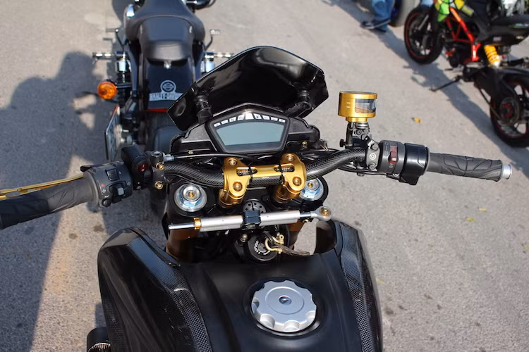 Không chỉ có dàn vỏ bằng sợi carbon, ngay cả ghi-đông của xe cũng được làm từ loại vật liệu siêu nhẹ này. Cùm ghi-đông bằng nhôm nhuộm vàng của CNC Racing thay cho cùm nguyên bản của Hypermotard, hai bên tay lái là cặp bao tay Spider mềm trong khi bình dầu phanh nguyên bản của xe đã được thay bằng bình Rizoma Next.