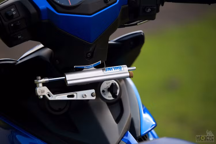 Ở bên dưới cổ xe, một cây trợ lực Ohlins đã được gắn thêm một cách khéo léo vào Exciter bằng pát "thửa riêng" và khoét nhựa gáy của xe. Cùng với cặp bánh lớn, trợ lực lái khiến cảm giác điều khiển của chiếc xe trở nên càng đầm chắc hơn.