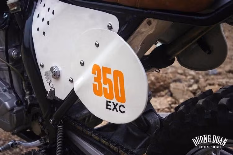 Trong khi đó, 2 bên thân xe cũng đã được DuongDoan cắt những tấm nắp che và bảng số theo đúng phong cách xe đua đường đất cổ điển. Toàn bộ các chi tiết thân xe có màu trắng, kết hợp cùng những họa tiết và chữ số đơn giản màu cam sáng theo đúng phong cách của hãng xe KTM.