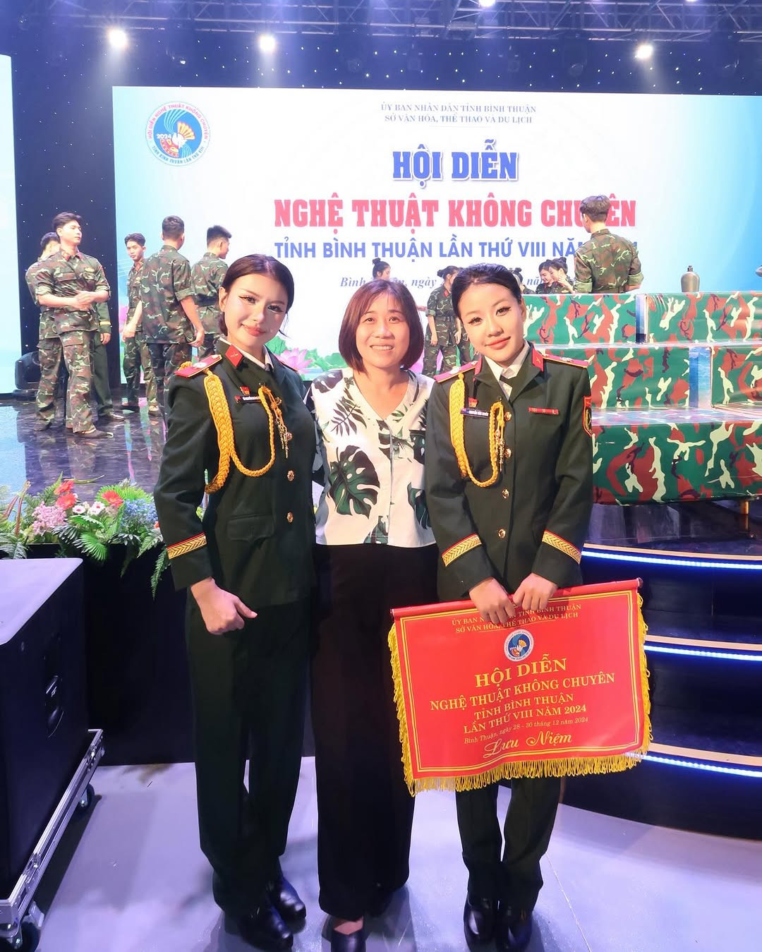 Theo đó, nữ Tiktoker diện quân phục, khoe dáng rạng rỡ. Phía sau là sân khấu Hội diễn Nghệ thuật không chuyên tỉnh Bình Thuận.