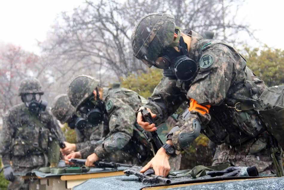 Tập tháo lắp vũ khí khi đeo mặt nạ phòng hóa. Mặt nạ phòng hóa có tầm nhìn rất hạn chế, nhất là trong thời tiết mưa phùn mắt kính của mặt nạ sẽ bị bám nước khiến người đeo bị giới hạn tầm nhìn rất nhiều. Nguồn ảnh: Sina.