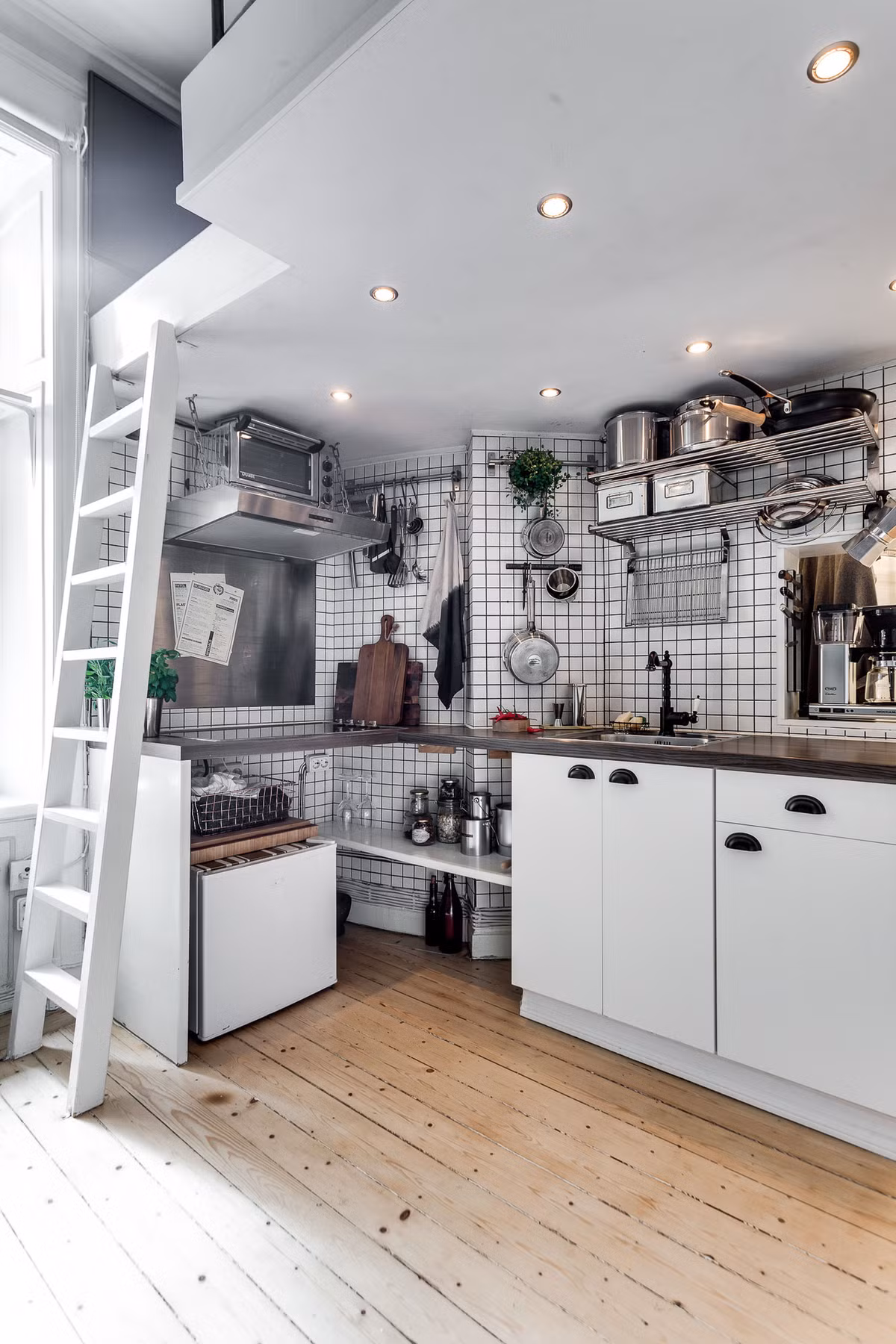 Phòng bếp nối thông với phòng khách theo hình chữ L. Toàn bộ phòng bếp đều sử dụng lưới bao quanh tường để có thể tiện treo đồ. Ngoài việc lắp thêm các kệ mở ở phía trên, các tủ ngăn kéo để lưu trữ đồ, chủ nhà còn lắp thêm kệ mở bên dưới mặt bếp để tăng thêm không gian lưu trữ.