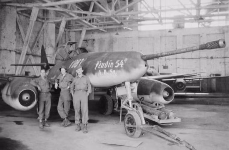 Mặc dù bị ném bom liên tục, tuy nhiên người Đức vẫn nỗ lực sản xuất được khoảng 1.400 chiếc Me 262 không chỉ có một phiên bản mà là hàng loạt phiên bản cải tiến khác nhau (15 mẫu cải tiến). Trong ảnh, phiên bản thử nghiệm Me-262 A-1a/U4 lắp pháo BK5 50mm ở đầu mũi có tốc độ bắn 940 phát/phút, cơ số đạn dược 22 viên, bị lính Mỹ bắt trong nhà máy ở Augsburg. Nguồn ảnh: WHO