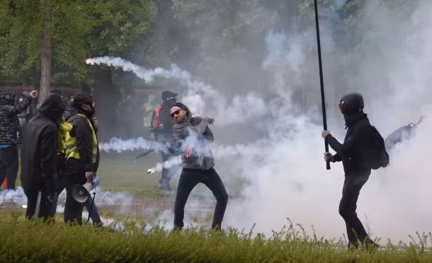 Một người biểu tình ném trả lựu đạn hơi cay về phía cảnh sát. Ảnh: The Sun.