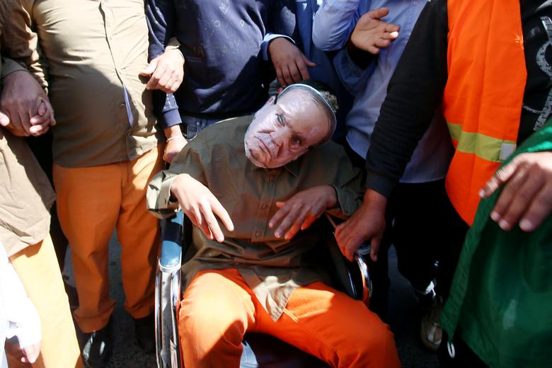 Một người đàn ông ngồi trên xe lăn và đeo mặt nạ hình Tổng thống Abdelaziz Bouteflika tham gia cuộc biểu tình ở Algiers.