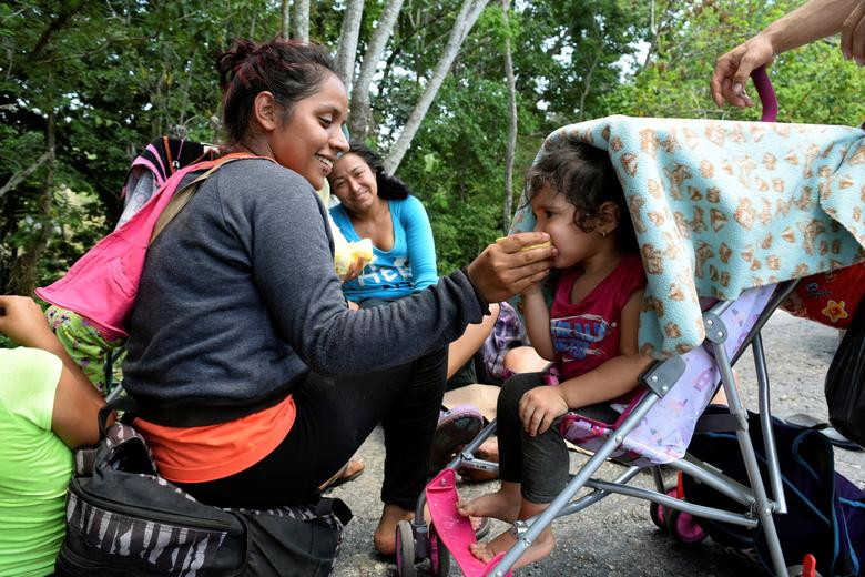 Một phụ nữ cho con ăn khi cùng các di dân khác ngồi nghỉ ven đường cao tốc ở Escuintla, bang Chiapas, Mexico, ngày 26/3.