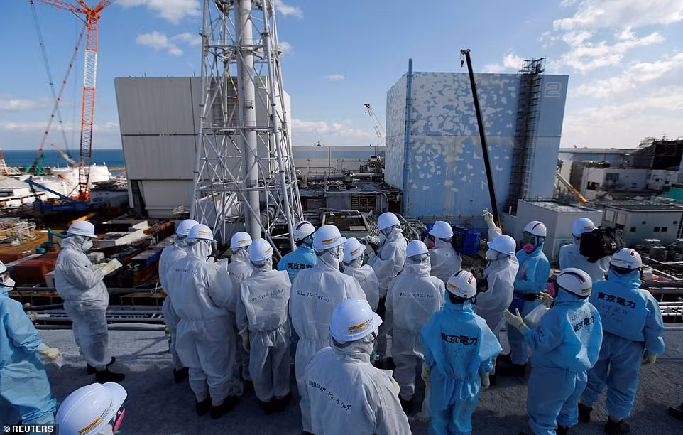 Các phóng viên và kỹ sư mặc đồ bảo hộ đứng trước lò phản ứng số 1 và số 2 tại nhà máy điện hạt nhân Fukushima. "Chúng tôi cuối cùng cũng bắt tay vào việc tái xây dựng", Thị trưởng Okuma Toshitsuna Watanabe nói với các phóngviên.