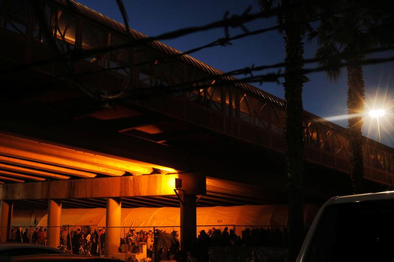 Các di dân đến từ khu vực Trung Mỹ xếp hàng chờ nhận đồ ăn được phân phát trong cơ sở giam giữ này.