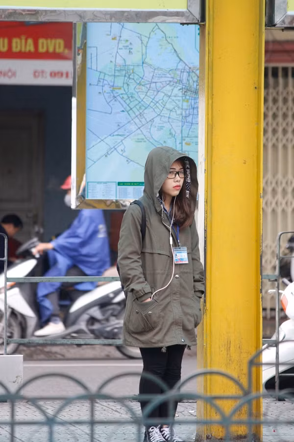 Nữ sinh đứng nép mình ở một góc cột đợi chờ xe buýt.