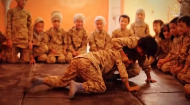 2 bé trai vật lộn trên sàn nhà ở ngôi trường của Nhà nước Hồi giáo, ở đây chúng còn được dạy cách sử dụng súng AK-47.
