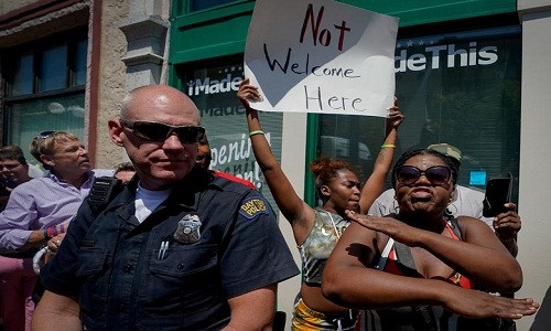 Người phụ nữ mang theo tấm biển với nội dung: "Ở đây không chào đón (ông Trump)".