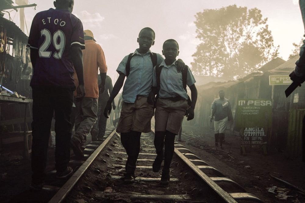 Hai nam sinh đi học về trên tuyến đường sắt nối thủ đô Nairobi và thành phố Kisumu ở hồ Victoria, được xây dựng từ năm 1901 dưới thời đất nước còn là thuộc địa của Anh. Vào đầu thế kỷ 20, chính phủ Anh cho phép các binh sĩ Kenya sinh sống ở khu vực đất công hai bên đường tàu, dẫn tới sự hình thành của khu ổ chuột Kibera. Ảnh: Anwar Sadat Swaka/The Guardian.