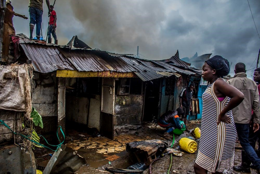 Một người phụ nữ đứng nhìn ngôi nhà kiêm cửa hàng của mình bị phá hủy bởi một đám cháy vừa mới được dập tắt trước đó. Hỏa hoạn là chuyện "như cơm bữa" ở khu ổ chuột Kibera. Ảnh: Anwar Sadat Swaka/The Guardian.