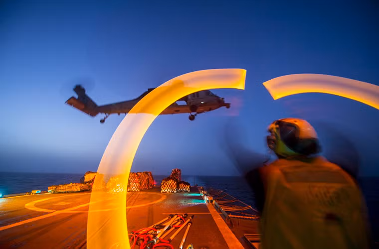 Hình ảnh thủy thủ trên tàu tàu khu trục mang tên lửa USS Philippine Sea (CG 58) hướng dẫn một chiếc trực thăng vận tải MH-60 đáp xuống sàn đáp trực thăng sau khi hoàn tất việc chuyển hàng tiếp tế.