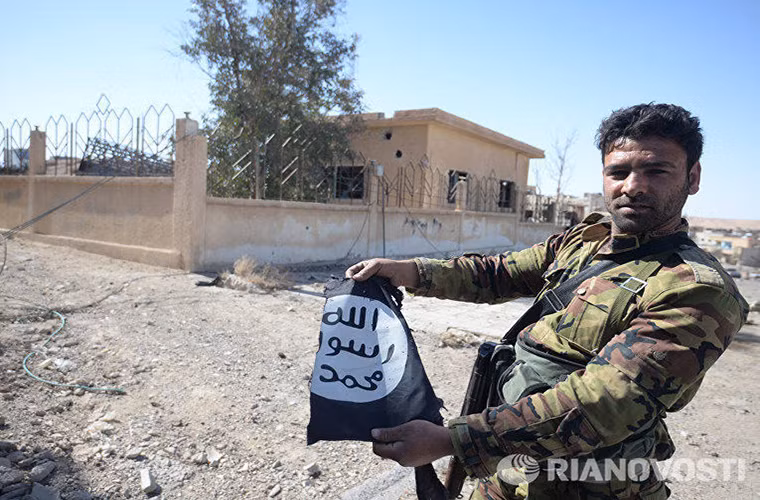 Một binh sĩ Syria tiến vào giải phóng Al-Qaryatayn trên tay là lá cờ bị xé nát của IS. Nguồn ảnh: Ria Novosti