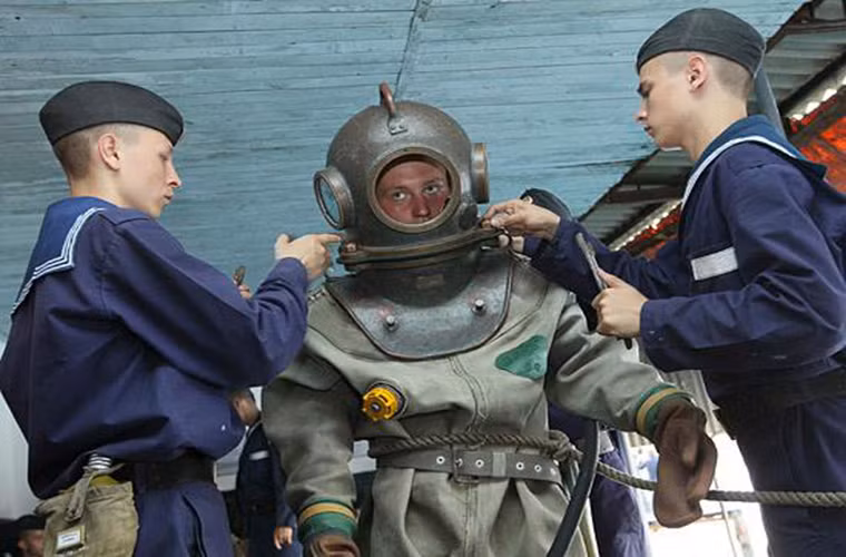 Tất nhiên với khối thiết bị nặng hàng trăm kg mang theo mỗi thợ lặn đều không thể mang được đồ nếu không có sự trợ giúp của đội hổ trợ trên mặt đất. Và bộ phận quan trọng nhất của mỗi đồ lặn là mũ lặn bằng kim loại cung cấp không khí cho thợ lặn khi dưới nước.