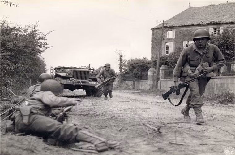 Hình ảnh bốn binh sĩ Mỹ cố gắng chạy về hai bên đường để tránh hỏa lực bắn thẳng từ súng máy của quân Đức ở một con dốc tại Normandy.