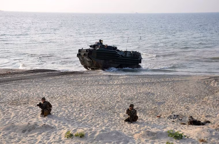 Dưới bờ biển là đội hình xe bọc thép lội nước LVTP-7 của Lính thủy Đánh bộ Mỹ đang tiến lên bờ biển.