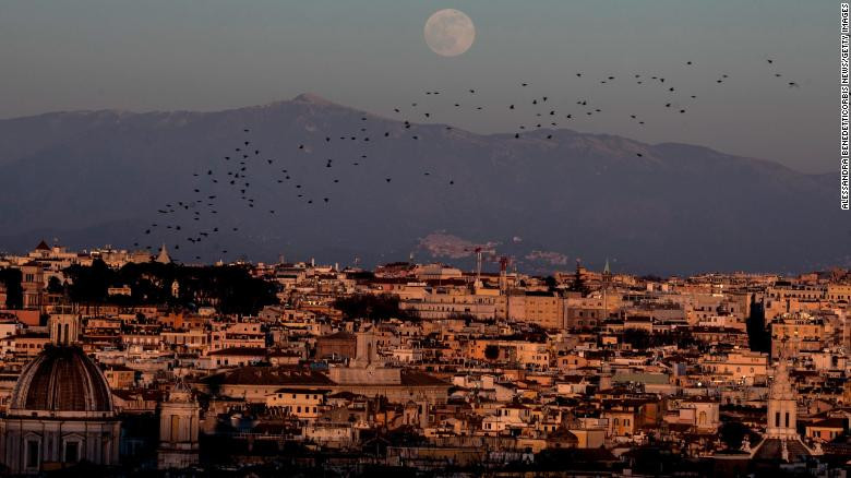 Đàn chim sáo bay trên bầu trời khi trăng mọc ở thành phố Rome, Italy.