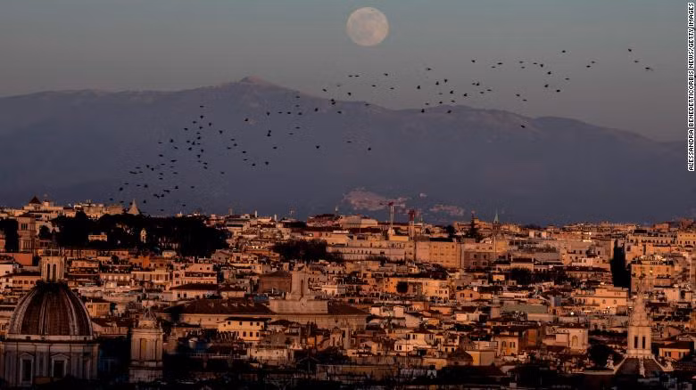Đàn chim sáo bay trên bầu trời khi trăng mọc ở thành phố Rome, Italy.