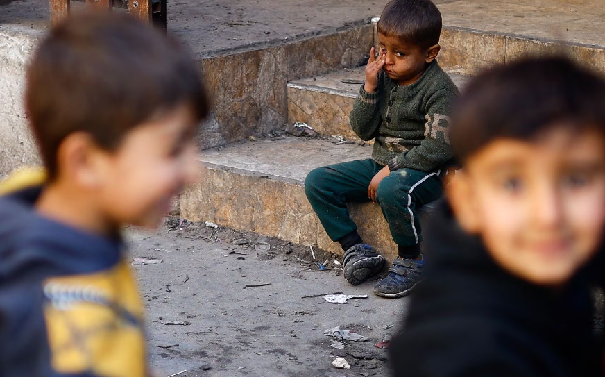 Một em nhỏ ngồi chờ trong lúc mọi người xếp hàng nhận đồ ăn ở Rafah hôm 16/1.