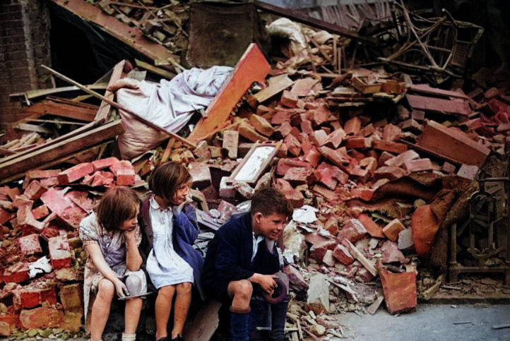 Các em nhỏ ngồi trước đống đổ nát ở Đông London, Anh. Nhiều ngôi nhà đã bị phá hủy trong vụ đánh bom của Đức Quốc xã trong trận Blitz năm 1940-1941.