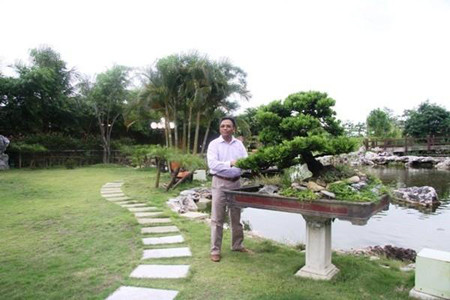 Ảnh chụp ông Cao Tiến Đoan bên ao cá và cây cảnh đắt tiền trong vườn.