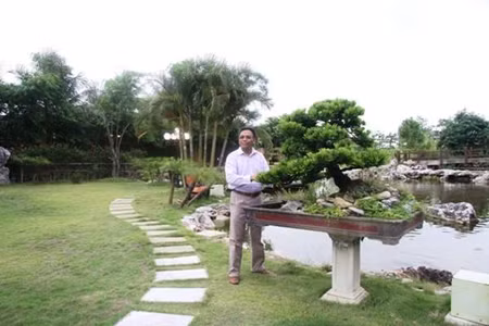 Ảnh chụp ông Cao Tiến Đoan bên ao cá và cây cảnh đắt tiền trong vườn.