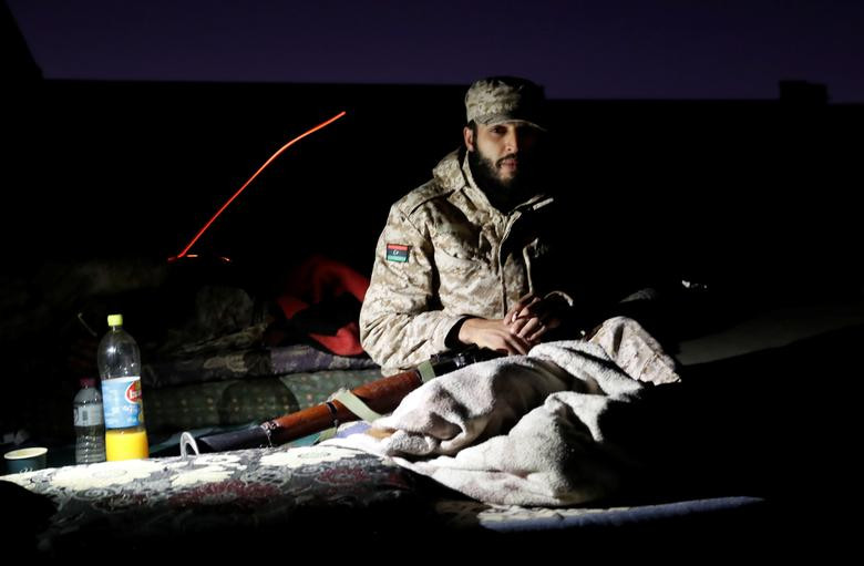 Tay súng GNA ôm vũ khí ngồi trên một tòa nhà ở Tripoli đêm 12/5 khi các cuộc giao tranh với lực lượng LNA vẫn chưa kết thúc.