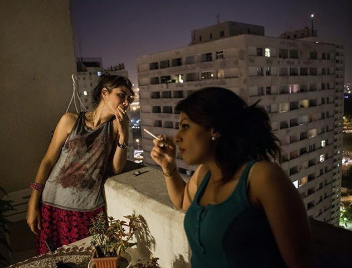 Hai người phụ nữ Iran đứng hút thuốc và trò chuyện ngoài ban công.