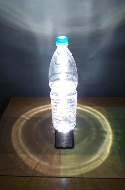  9. Dùng đèn flash trên điện thoại làm đèn bàn. Việc dùng đèn flash trên điện thoại làm đèn pin không còn là điều quá mới mẻ, tuy nhiên bạn có thể cải thiện đèn flash trên thiết bị của mình thành một chiếc đèn để bàn (hay thậm chí là đèn ngủ nếu thiết bị "dư pin") bằng cách đặt một chai nước (có nước bên trong) để đứng ngay bên trên chiếc đèn flash ấy.