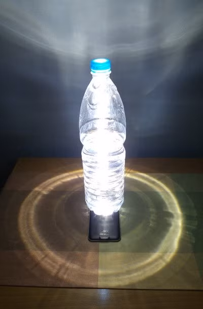  9. Dùng đèn flash trên điện thoại làm đèn bàn. Việc dùng đèn flash trên điện thoại làm đèn pin không còn là điều quá mới mẻ, tuy nhiên bạn có thể cải thiện đèn flash trên thiết bị của mình thành một chiếc đèn để bàn (hay thậm chí là đèn ngủ nếu thiết bị "dư pin") bằng cách đặt một chai nước (có nước bên trong) để đứng ngay bên trên chiếc đèn flash ấy.