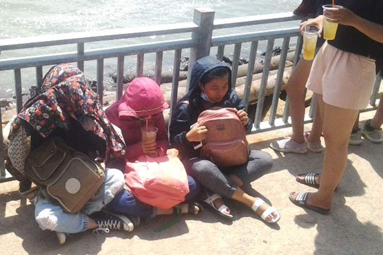 Một số khách du lịch mỏi mệt ngồi giữa nắng trưa gay gắt chờ tàu đò.