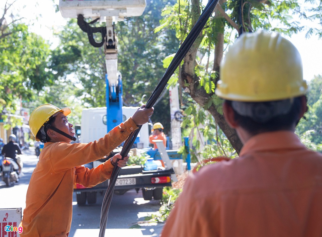 Ngày 23/9, nhiều công nhân đang đấu nối dây điện bị đứt. Những nơi chưa có cột điện mới thay thế, họ phải gác tạm dây lên cây xanh ven đường.