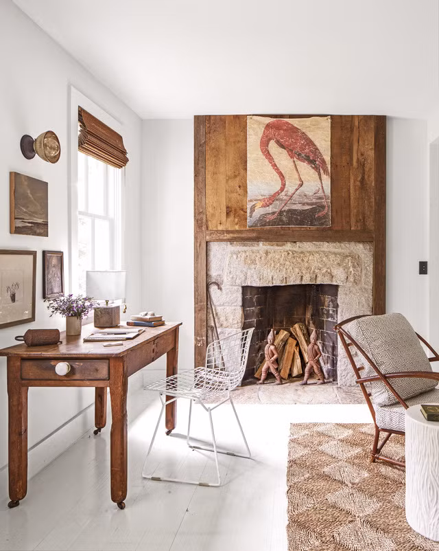 Do không có đủ diện tích để dành riêng một phòng làm việc , nên chủ nhà chỉ kê một chiếc bàn gỗ đơn giản gần cửa sổ để lấy ánh sáng và một chiếc ghế kim loại mắt lưới màu trắng giản đơn. Bếp sưởi được làm từ đá granit, bên trên là một tấm bảng gỗ với bức tranh hình con hồng hạc. Ảnh: Countryliving.