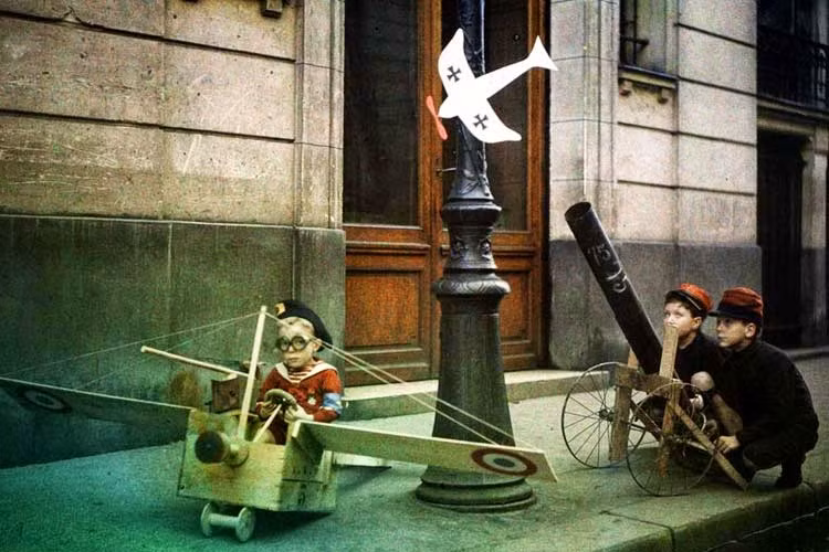 Một nhóm trẻ em vui đùa với những món đồ chơi hiện đại. Trong đó, có bé trai ngồi lên máy bay gỗ thử tài làm phi công. Đằng sau là hai bé trai lớn tuổi hơn đang đóng giả làm binh lính tiêu diệt máy bay địch.