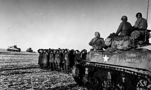 Lính Mỹ ngồi trên xe tăng trong khi những tù binh chiến tranh Đức bị bắt đứng gần đó.