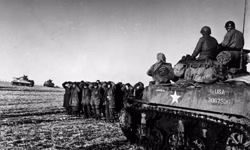 Lính Mỹ ngồi trên xe tăng trong khi những tù binh chiến tranh Đức bị bắt đứng gần đó.
