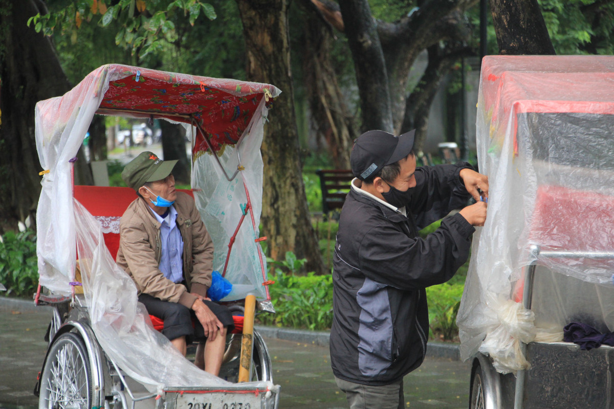 Trời mưa, gió rét nên khu vực hồ Hoàn Kiếm không có khách dạo phố nhưng những người chạy dịch vụ xích lô vẫn cố bám trụ trên đường và chống chọi mưa rét bằng cách chằng buộc áo mưa xung quanh xe.