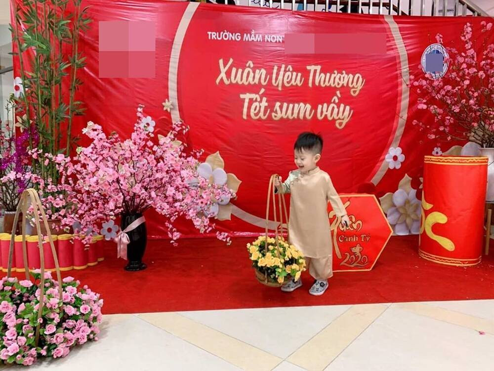 Con trai Việt Anh, bé Đậu Đậu mặc áo dài vàng, tay cầm giỏ hoa giữa phông nền đỏ đậm chất Tết.