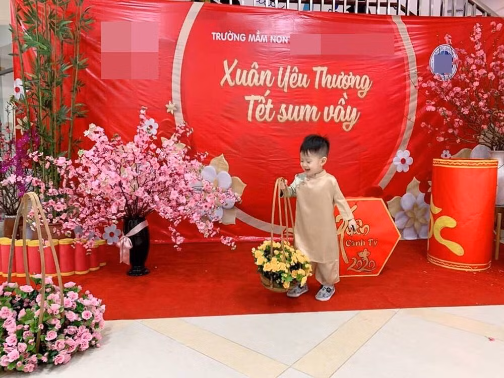 Con trai Việt Anh, bé Đậu Đậu mặc áo dài vàng, tay cầm giỏ hoa giữa phông nền đỏ đậm chất Tết.