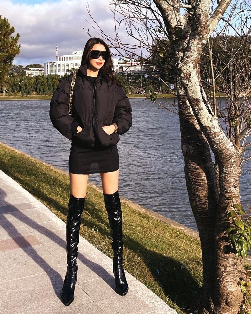 Dạo phố ngày đông lạnh, Trà Ngọc Hằng phối trang phục nguyên màu đen gồm đầm xuyên thấu với áo phao ấm áp và đôi boot đen sang chảnh.