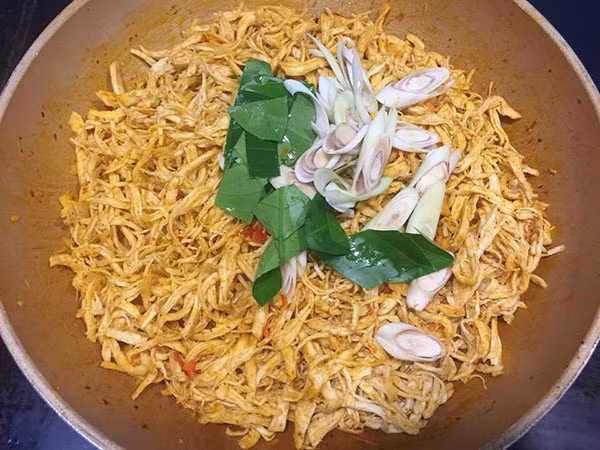 Đun nóng 3 thìa dầu ăn, cho hạt điều vào chưng cho có màu đỏ đẹp, vứt bỏ xác. Cho tỏi và ớt sừng vào phi thơm, sau đó cho tiếp phần còn lại của bột ngũ vị hương, bột ớt Hàn Quốc vào xào trong vài phút. Khi hỗn hợp có màu đẹp cho thịt gà đã xé cùng với sả và lá chanh cắt xéo vào. Hạ lửa nhỏ, đảo đều cho gà thấm gia vị khoảng 5-7 phút.