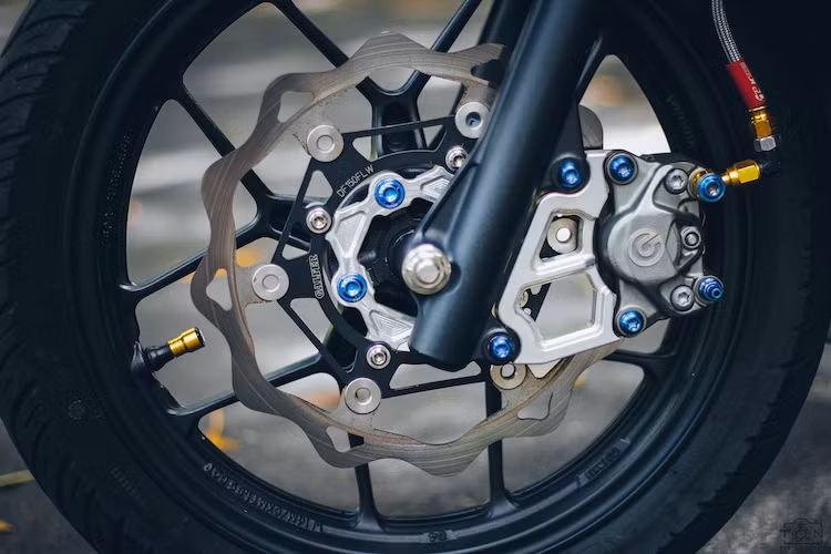 Ở bánh trước, bộ mâm 5 cánh kép nguyên bản của Vario được giữ lại, nhưng sử dụng lốp Michelin bám đường hơn. Trong khi đó, hệ thống phanh được nâng cấp bằng dây dầu K-Tech, đĩa hoa Galfer, heo Brembo 2 pis đối xứng và bắt vào phuộc bởi dàn ốc titan màu xanh bắt mắt.