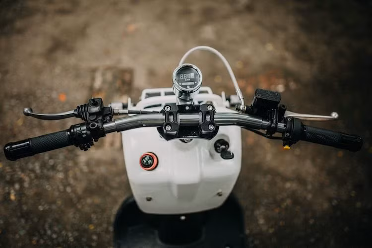 Toàn bộ hệ thống phuộc và bánh trước của chiếc Zoomer nguyên bản được giữ nguyên, với thay đổi duy nhất là hệ thống phanh được nâng cấp lên phanh đĩa. Ở phía trên tay lái, ghi-đông cao nguyên bản của chiếc xe đã được thay bằng tay lái rộng ngang dạng dragbar, phía trên là đồng hồ cùng cùm công tắc tối giản và bao tay Rizoma Lux.