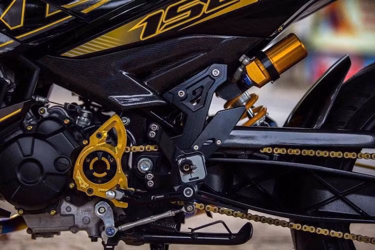 Chưa dừng lại ở đó, chủ xe còn thay "mang cá" chắn nhông nguyên bản bằng loại nhôm CNC của hãng Bikers. Dàn để chân trên xe đã được thay bằng số gảy Rizoma cũng được làm từ nhôm siêu nhẹ. Để tăng tính ổn định cho phần đuôi của chiếc xe khi vận hành, cây phuộc Ohlins bình dầu rời đã thay thế cho phuộc nguyên bản của Exciter.